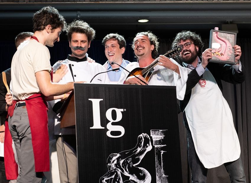 The research team on stage at the Ig Nobel ceremony, laughing, one holding a mandolin and another holding the prize